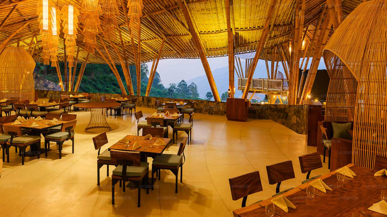 Open-air bamboo restaurant with warm lighting and mountain views, featuring wooden tables and chairs for guests.