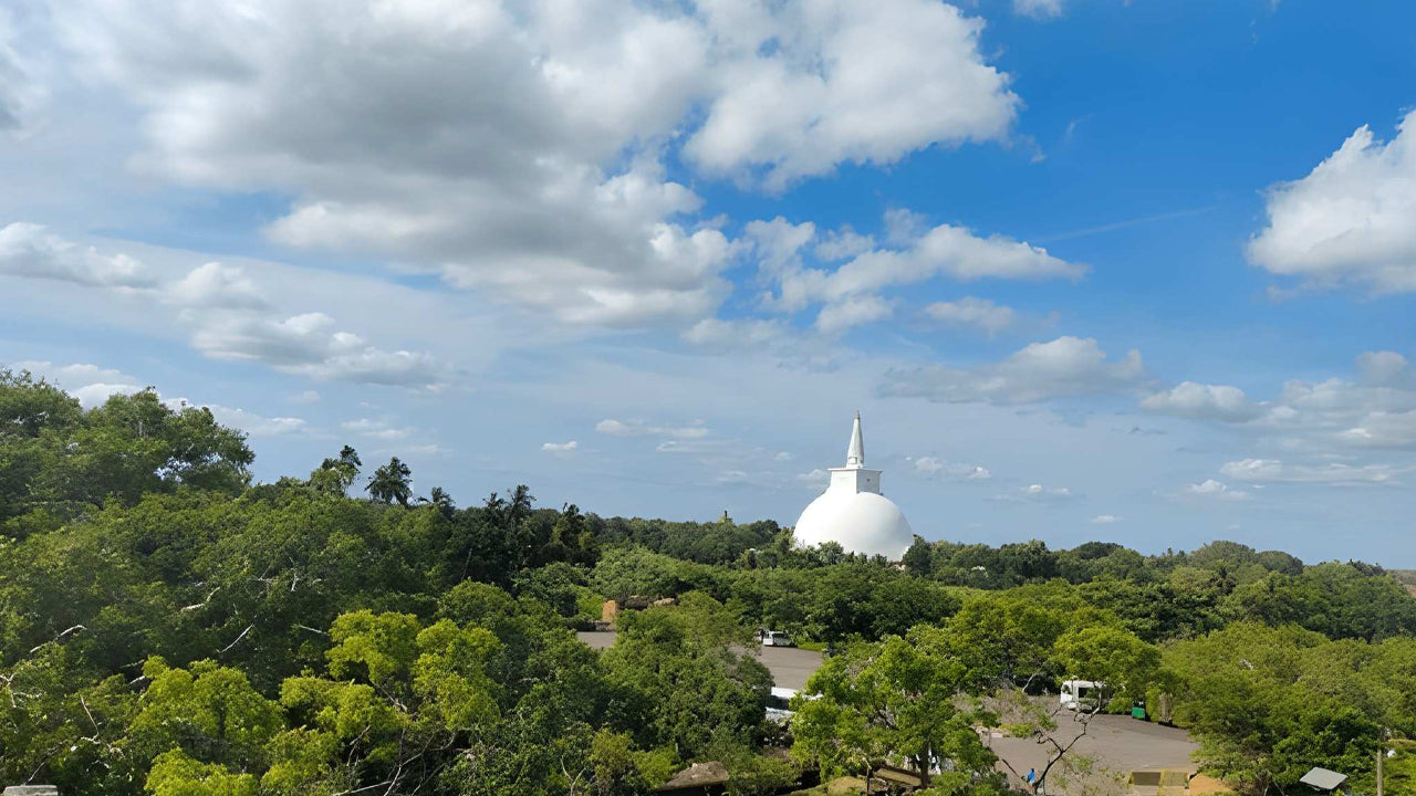 White stupa surrounded by green trees under a blue sky with clouds